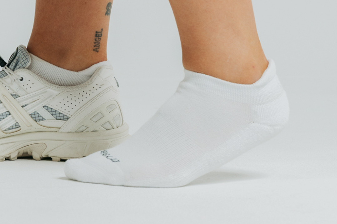 Woman in a white DryStep Ankle Tab sock beside a cream trail sneaker, studio shot