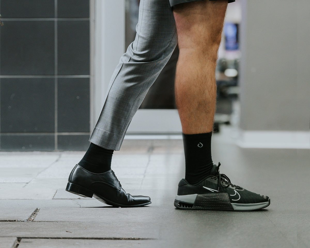 Man in black DryStep Crew socks, a dress shoe and suit on one leg, a Nike trainer on the other