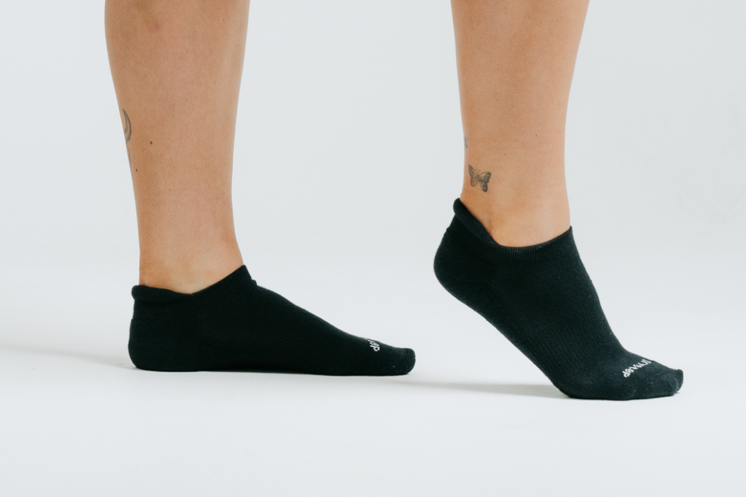 Woman standing in black DryStep Ankle Tab socks, one heel raised, studio shot