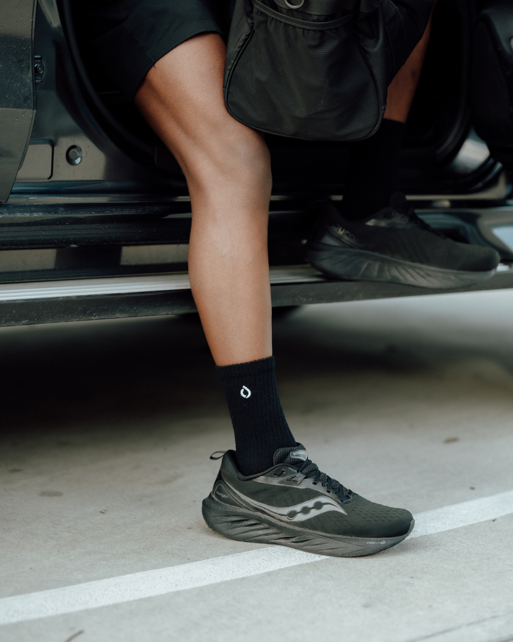 Black mid-crew sock worn with trainers, resting on a car sill