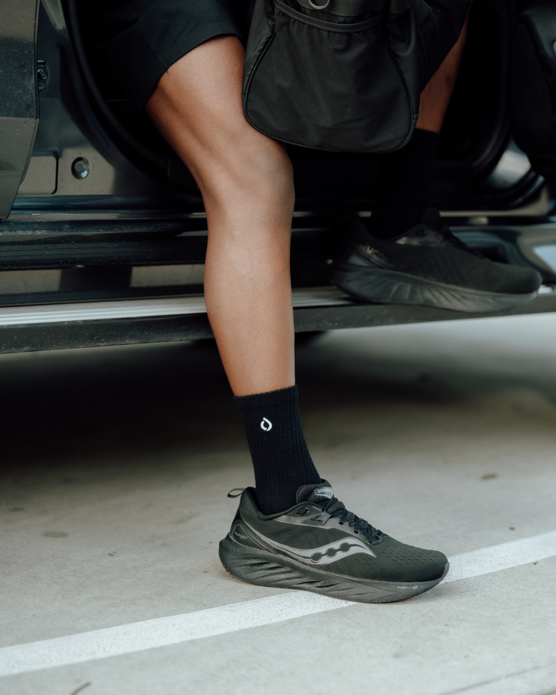 Black mid-crew sock worn with trainers, resting on a car sill