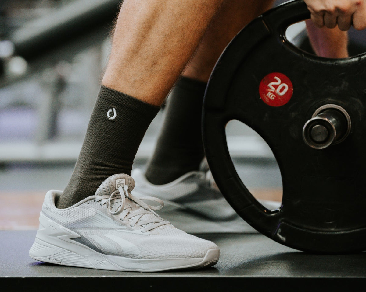 Man in dark grey DryStep Crew socks and white Reebok trainers loading a 20kg plate at the gym