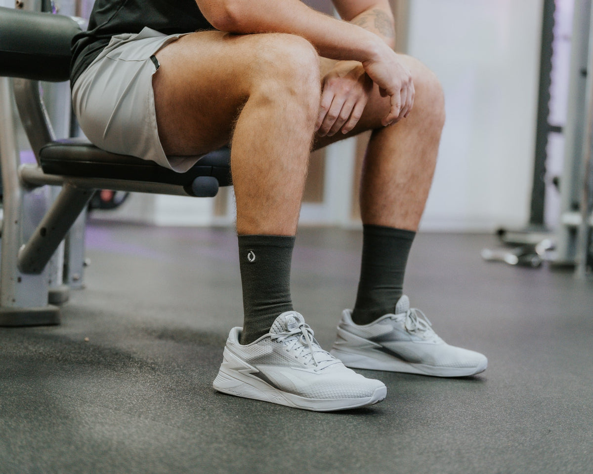 Man on a gym bench in dark grey DryStep Crew socks and white Reebok trainers