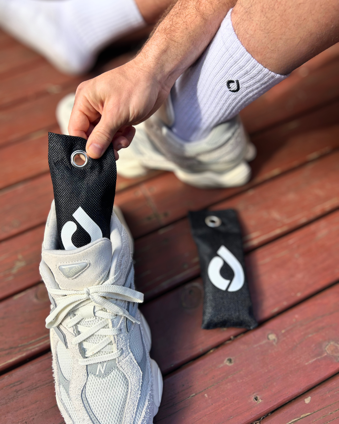 Man putting a DryStep charcoal shoe freshener into a white New Balance sneaker on a timber deck